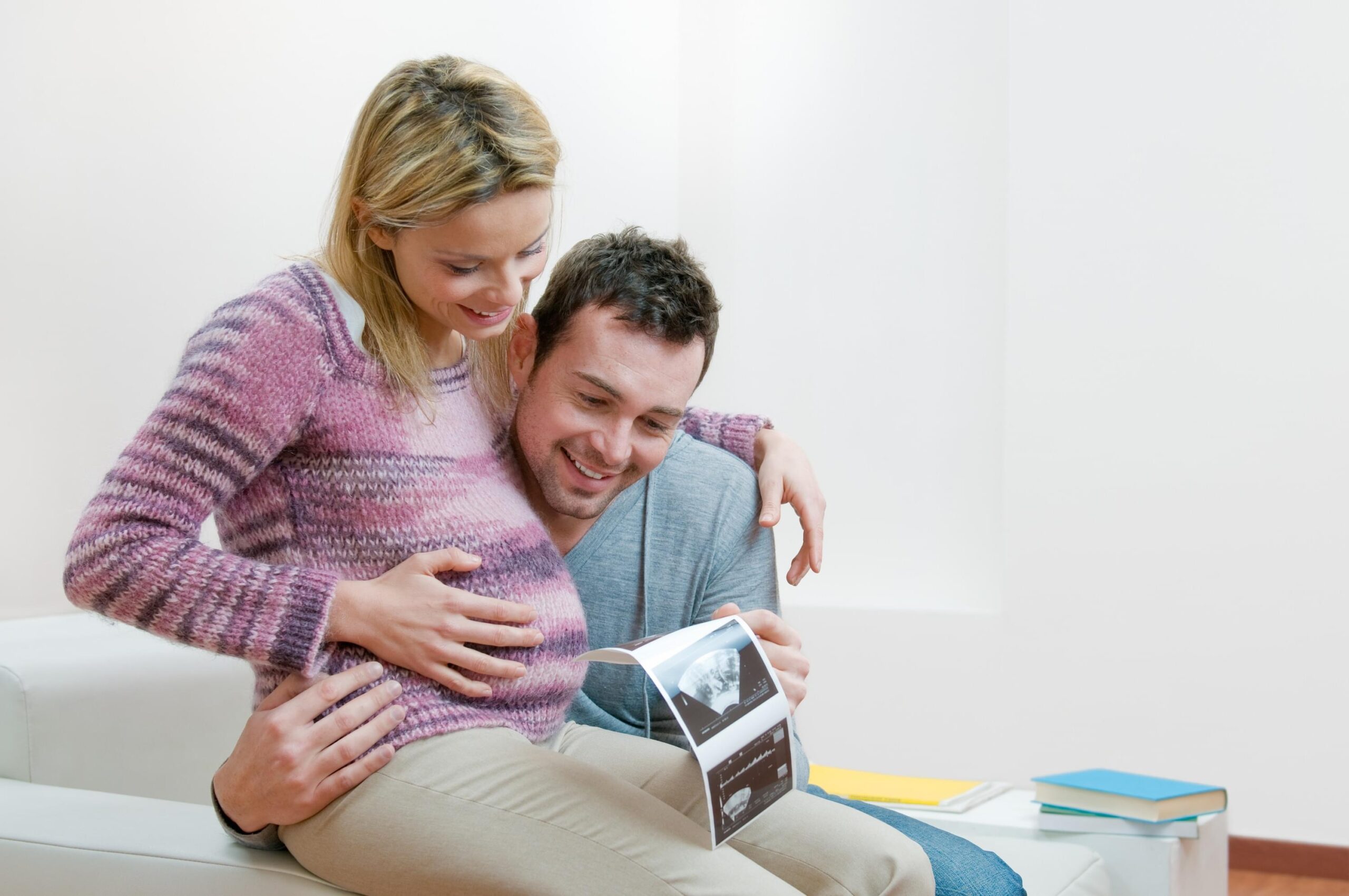 Happy pregnant young couple with baby sonogram Young smiling couple holding and looking at an ultrasound scan of their expecting baby at home, copy space
